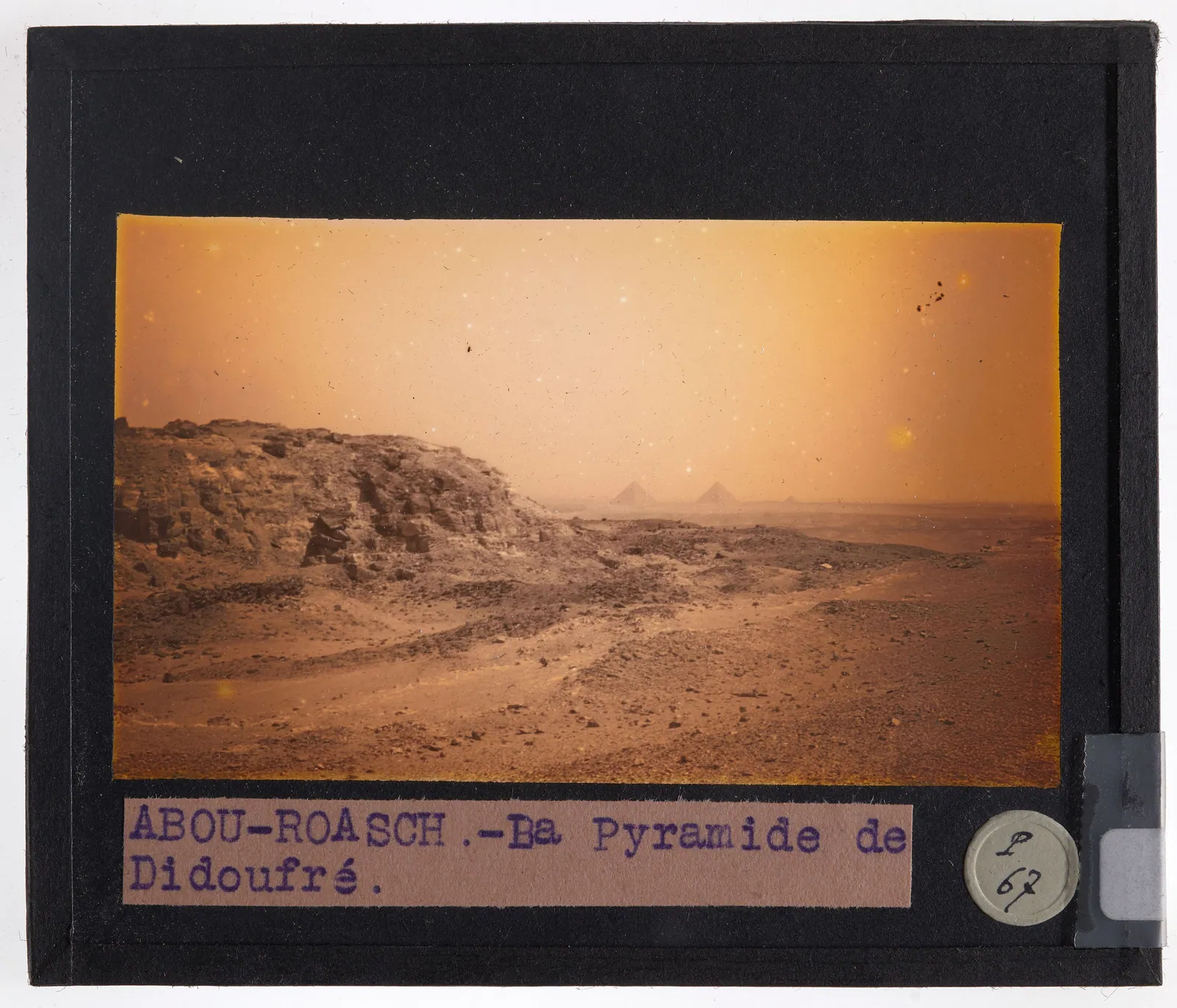 Handkolorerad skioptikonbild (Louvains universitet, tidigt 1900-tal), ”Abou-Roasch – La Pyramide de Didoufré”: Djedefres pyramidruin på sin höjd, med Gizas tre pyramider vid horisonten åtta kilometer bort.