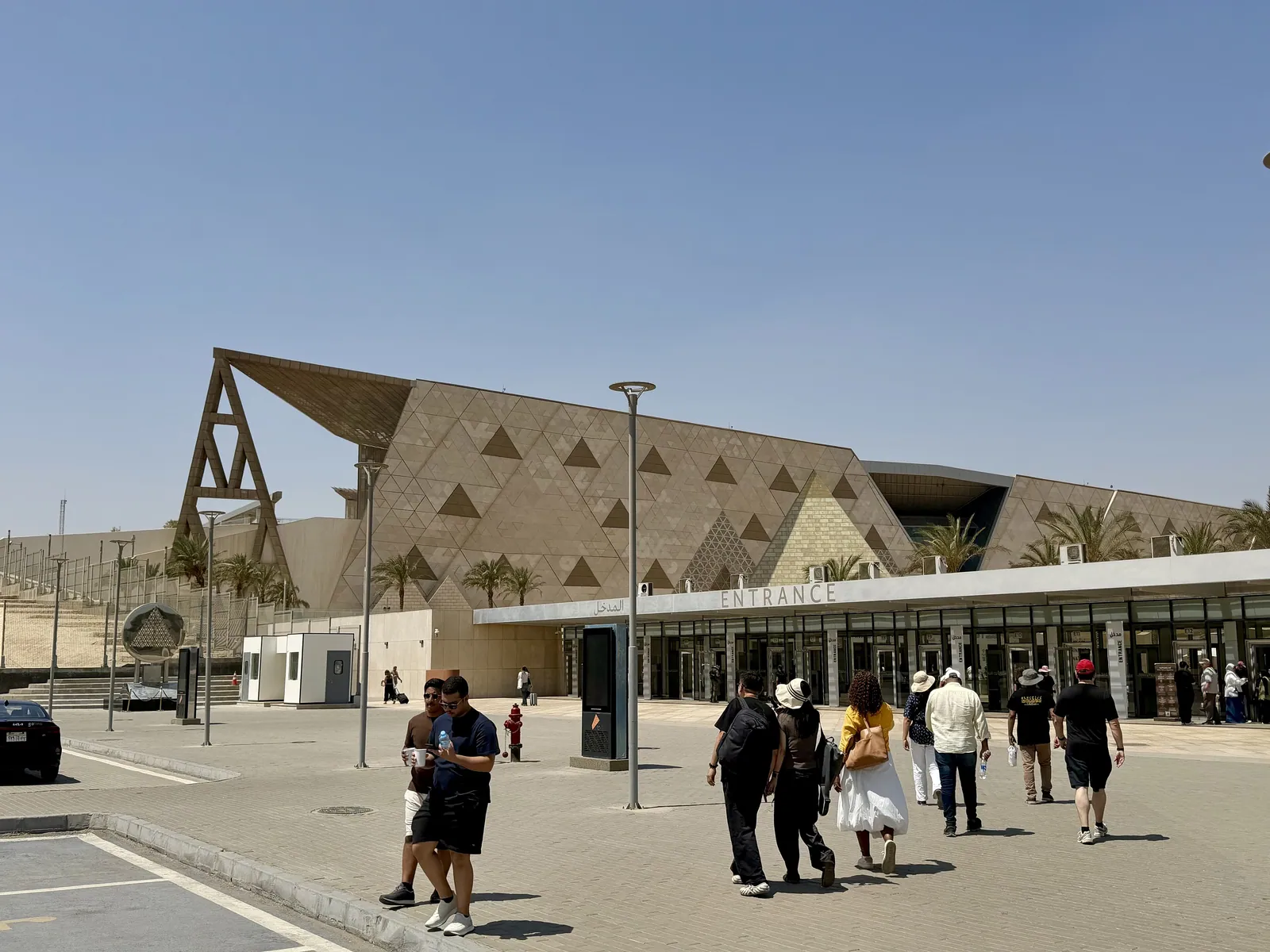 Stora egyptiska museets fasad av triangulerad sten (fotograferad i augusti 2026). Museet invigdes officiellt den 1 november 2025; resans guidade besök är dag 5, och på kvällen är fasaden upplyst på andra sidan vägen från hotellet.