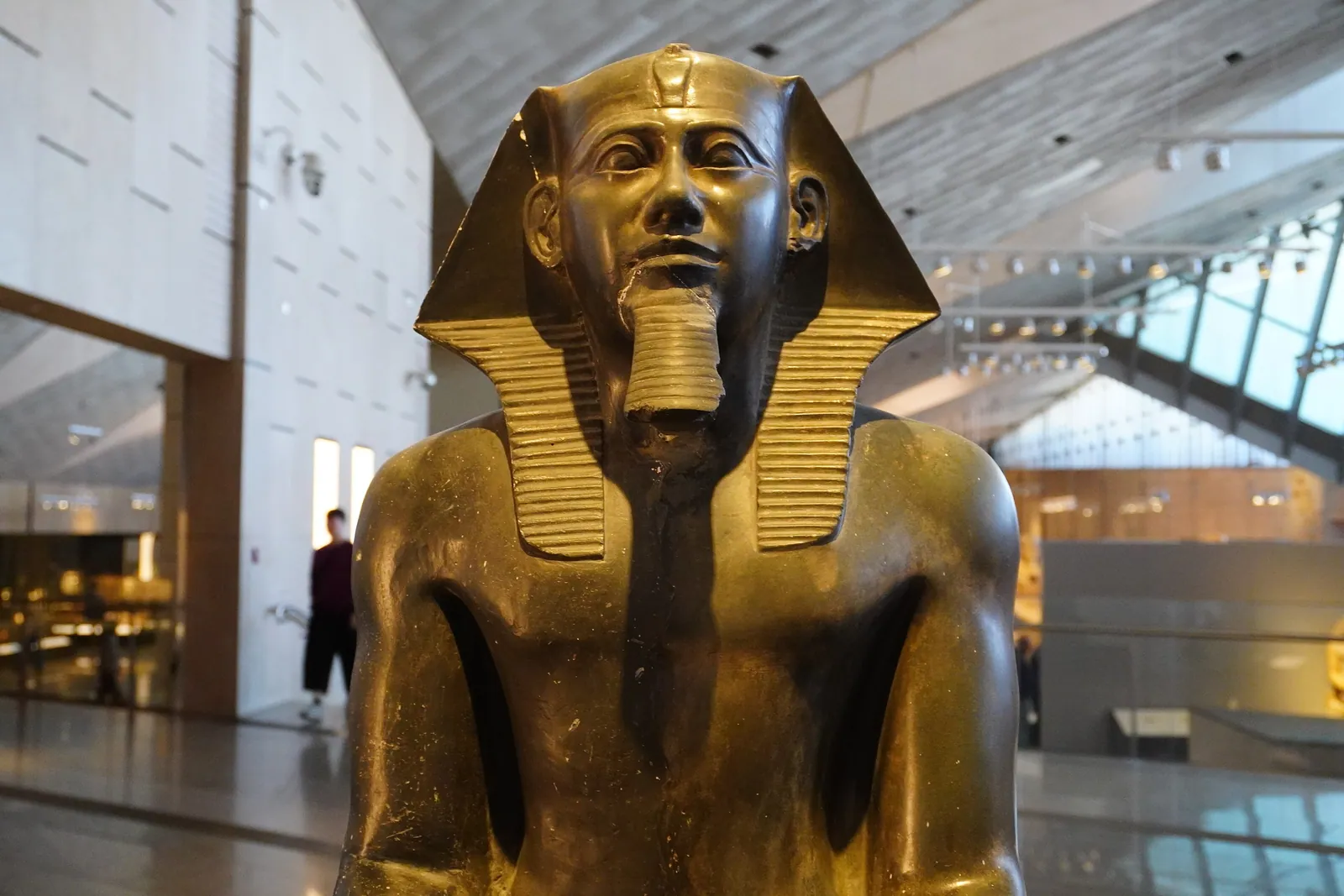 Sittande dioritstaty av Chefren från hans dalgångstempel i Giza, utställd på GEM (dec. 2025). Till skillnad från den berömda statyn med horusfalken, som finns kvar på Tahrir, saknar den falk bakom huvudet.