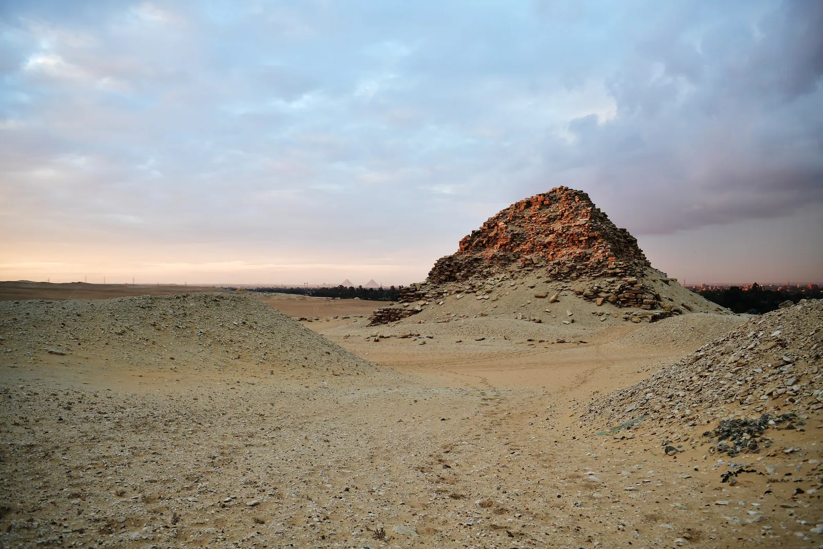 Sahures ruinerade pyramid (ca 2480 f.Kr.) i Abusir i det sista kvällsljuset – längst bort vid horisonten skymtar Gizapyramiderna. Den blottade kärnan visar det grova murverket med lerbruk som en gång doldes bakom en beklädnad av fin Turakalksten.