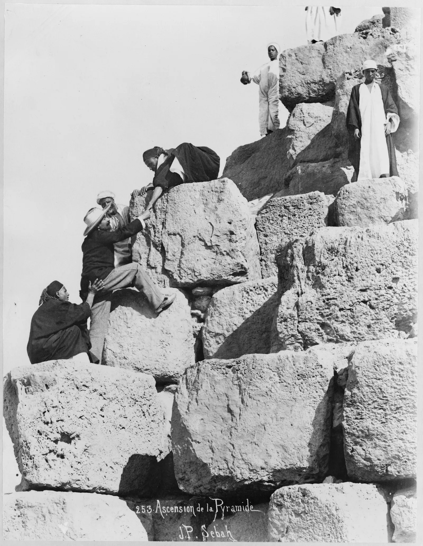 Pascal Sébah, ”Ascension de la Pyramide”, 1870-talet: en resenär i europeisk kostym knuffas och dras uppför Cheopspyramiden av lokala guider.
