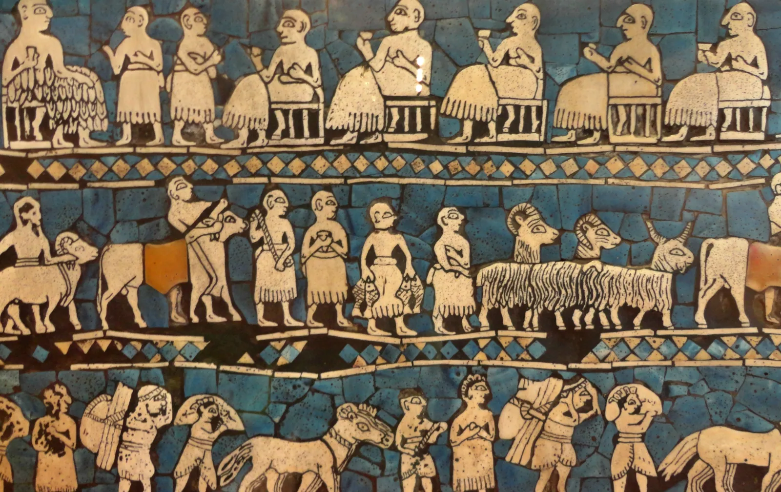 ”Fredssidan” av Urstandaret (British Museum): snäckskal, lapis lazuli och röd kalksten i bitumen från kungagravarna i Ur, ca 2600–2500 f.Kr. – ett gästabud och ett tåg med djur och varor, tillverkat i samma generation som pyramiderna i Giza.
